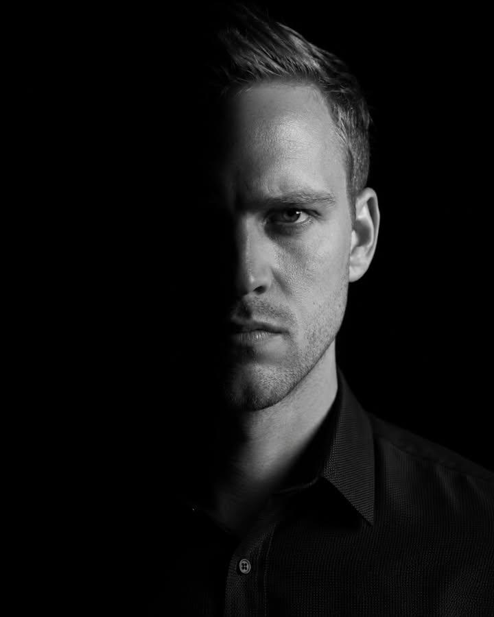 A dramatic, high-contrast low-key portrait of a subject. The